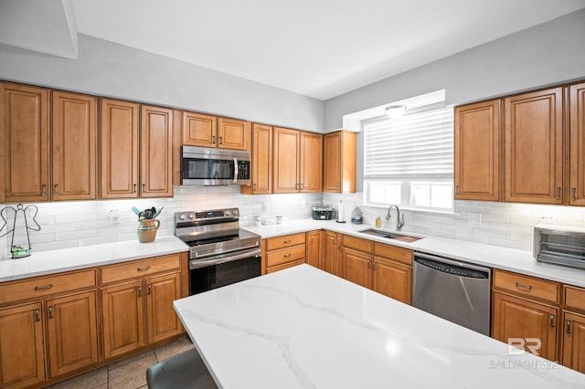 kitchen featuring light stone counters, brown cabinets, backsplash, appliances with stainless steel finishes, and a sink