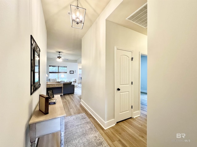 hallway with baseboards, light wood-style flooring, visible vents, and an inviting chandelier