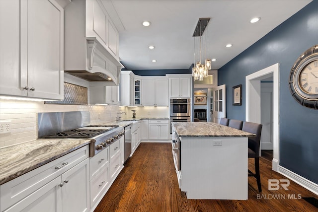 kitchen featuring pendant lighting, white cabinets, light stone counters, a kitchen island, and stainless steel appliances