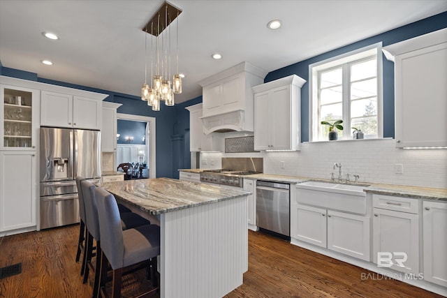 kitchen featuring appliances with stainless steel finishes, decorative backsplash, a kitchen island, decorative light fixtures, and dark wood-type flooring