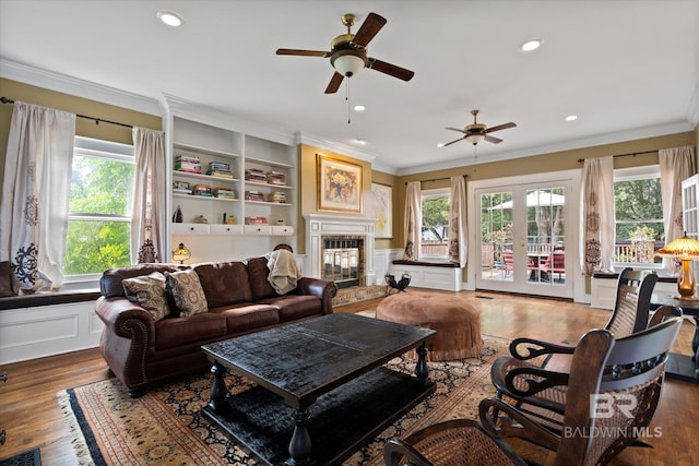 living room featuring wood-type flooring, french doors, built in shelves, a tile fireplace, and ornamental molding