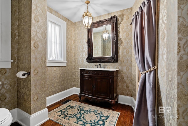 bathroom featuring hardwood / wood-style floors, toilet, vanity, and an inviting chandelier