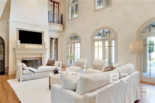 living room featuring light wood-type flooring, a high ceiling, french doors, and plenty of natural light