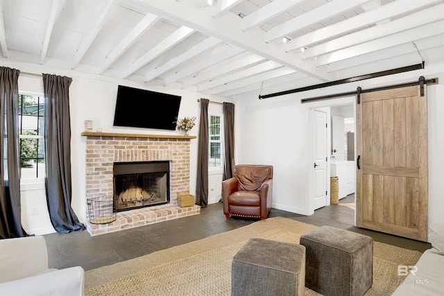 living room with a brick fireplace, beam ceiling, a barn door, and baseboards