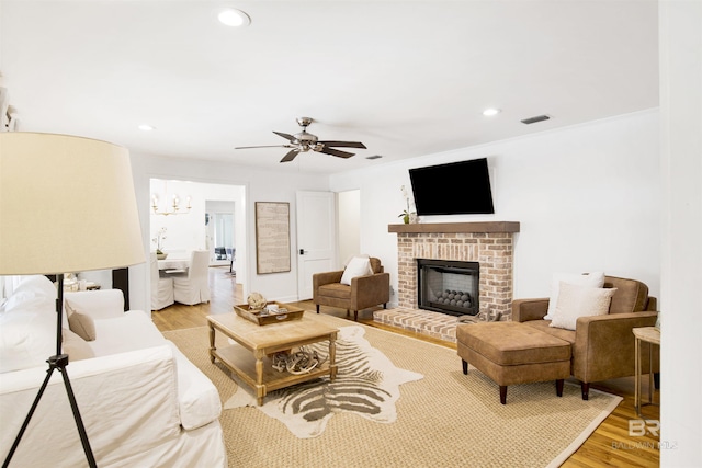 living room featuring recessed lighting, ceiling fan with notable chandelier, a fireplace, light wood finished floors, and visible vents