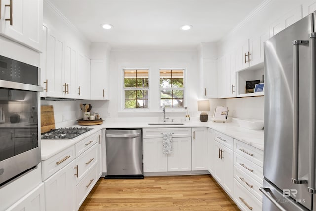 kitchen with appliances with stainless steel finishes, white cabinetry, crown molding, and a sink