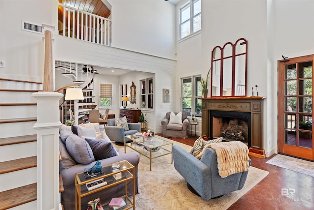 living area with stairway, decorative columns, a fireplace, concrete flooring, and a towering ceiling