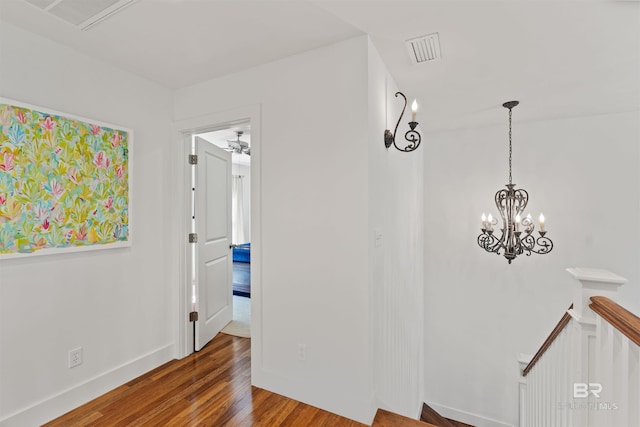 hallway with an upstairs landing, wood finished floors, visible vents, and baseboards