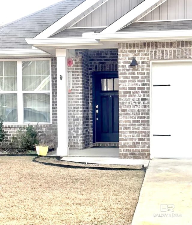 doorway to property with board and batten siding, brick siding, and a garage