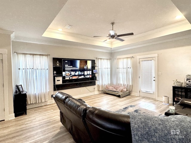 living room featuring ornamental molding, wood finished floors, baseboards, ceiling fan, and a raised ceiling