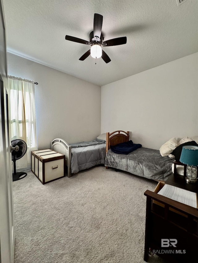 carpeted bedroom featuring ceiling fan and a textured ceiling