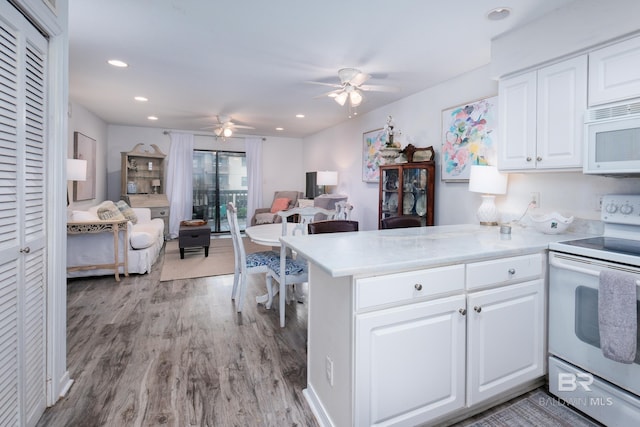 kitchen with light wood finished floors, a peninsula, white appliances, white cabinetry, and a ceiling fan