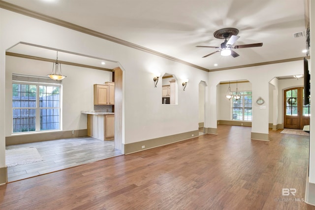 unfurnished living room featuring ceiling fan with notable chandelier, wood-type flooring, and ornamental molding