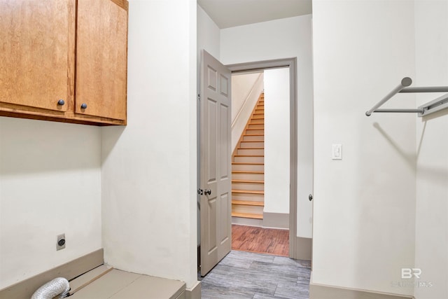 laundry area with electric dryer hookup, light hardwood / wood-style flooring, and cabinets