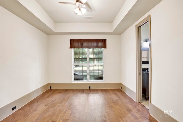 empty room with light hardwood / wood-style flooring, ceiling fan, and a raised ceiling