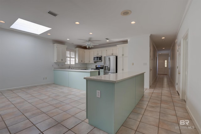 kitchen with white cabinets, a center island, appliances with stainless steel finishes, and light tile patterned flooring