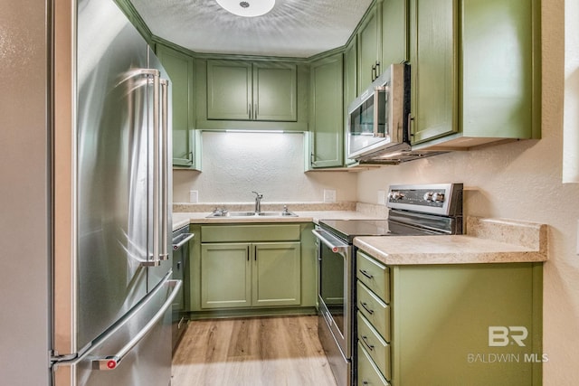 kitchen featuring sink, light hardwood / wood-style flooring, stainless steel appliances, a textured ceiling, and green cabinetry