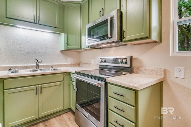 kitchen featuring appliances with stainless steel finishes, sink, green cabinets, and light wood-type flooring