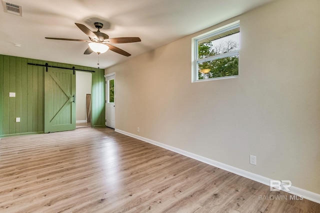 unfurnished room featuring a barn door, wooden walls, ceiling fan, and light hardwood / wood-style flooring