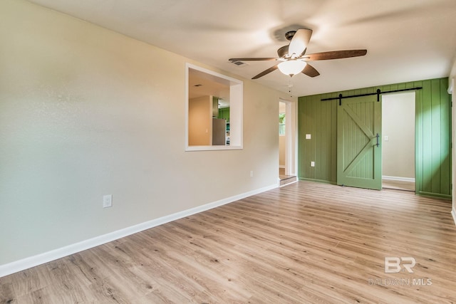 unfurnished room featuring light hardwood / wood-style floors, a barn door, and ceiling fan