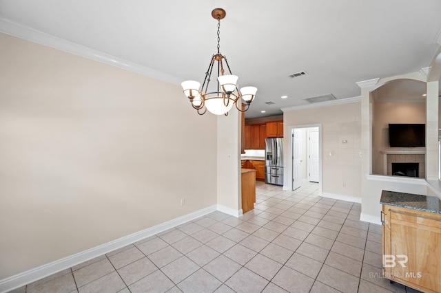 kitchen featuring a tile fireplace, light tile patterned flooring, an inviting chandelier, crown molding, and stainless steel fridge