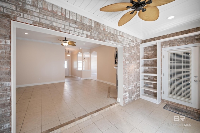 tiled spare room with ornamental molding, ceiling fan, and brick wall