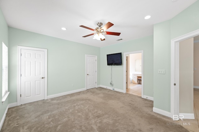 unfurnished bedroom featuring multiple windows, ensuite bath, ceiling fan, and light colored carpet