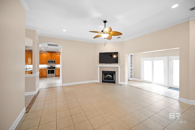 unfurnished living room featuring a tiled fireplace, ceiling fan, light tile patterned floors, and crown molding