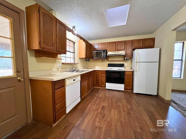 kitchen with a skylight, sink, white appliances, dark wood-type flooring, and a textured ceiling