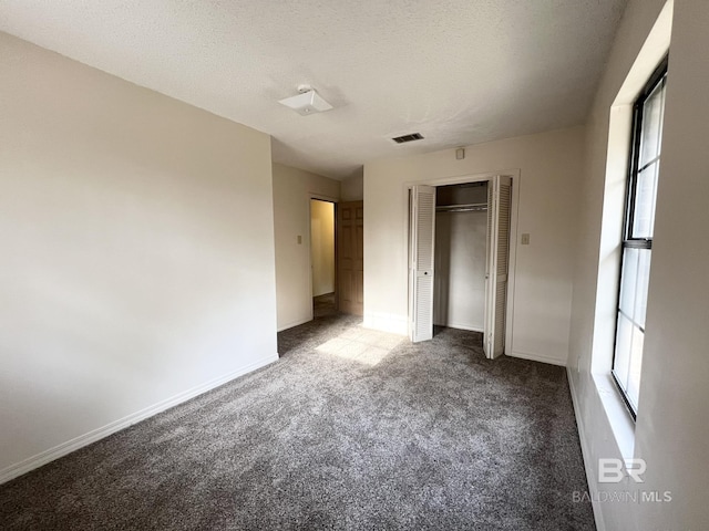 unfurnished bedroom with multiple windows, a textured ceiling, and dark colored carpet