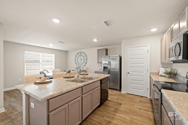 kitchen with gray cabinetry, sink, stainless steel appliances, light hardwood / wood-style floors, and a center island with sink