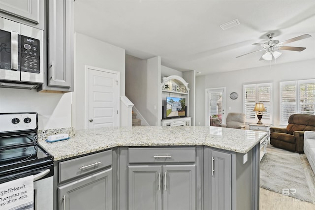 kitchen featuring ceiling fan, kitchen peninsula, light stone countertops, appliances with stainless steel finishes, and gray cabinetry