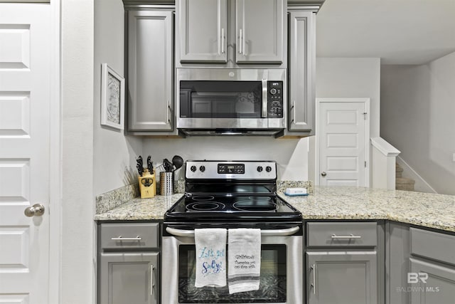 kitchen with appliances with stainless steel finishes, gray cabinetry, and light stone counters