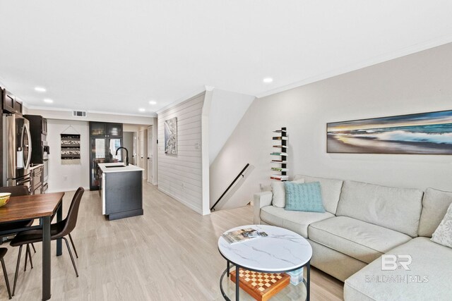 living room with light wood-type flooring, wooden walls, crown molding, and sink