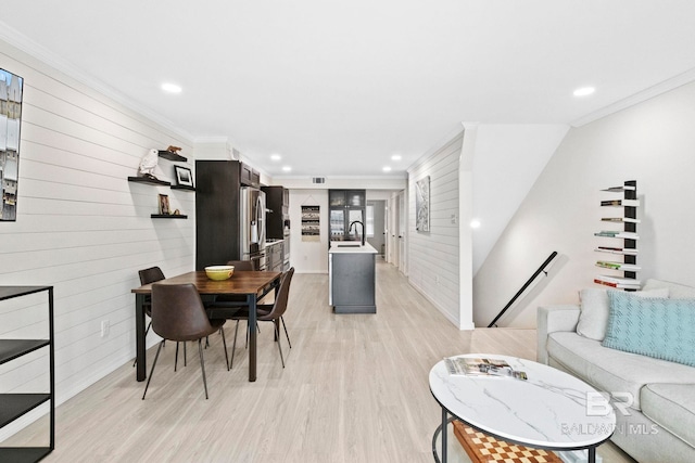 dining space with light hardwood / wood-style floors, crown molding, wood walls, and sink