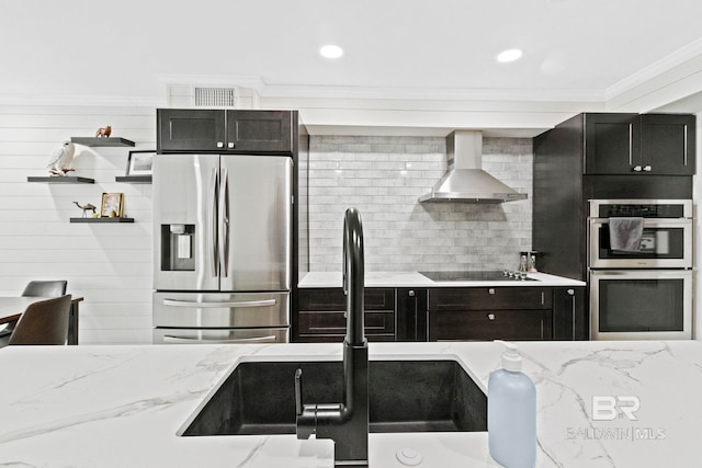 kitchen featuring stainless steel appliances, sink, ornamental molding, light stone countertops, and wall chimney range hood