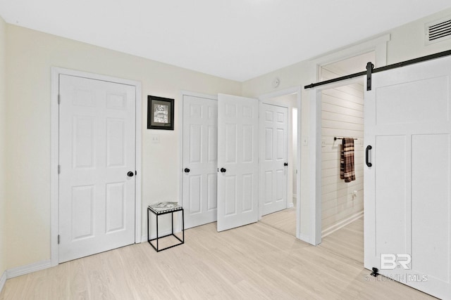 unfurnished bedroom featuring multiple closets, light hardwood / wood-style floors, and a barn door