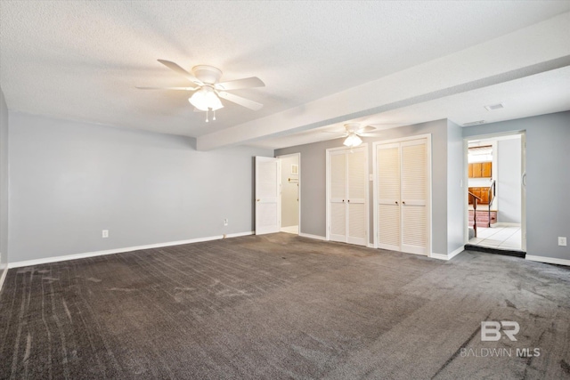 unfurnished bedroom with ceiling fan, a textured ceiling, carpet floors, and two closets