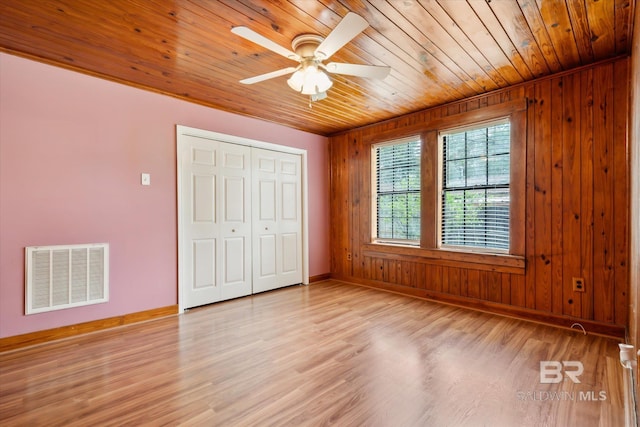 unfurnished bedroom with ceiling fan, wooden ceiling, light hardwood / wood-style floors, a closet, and wooden walls