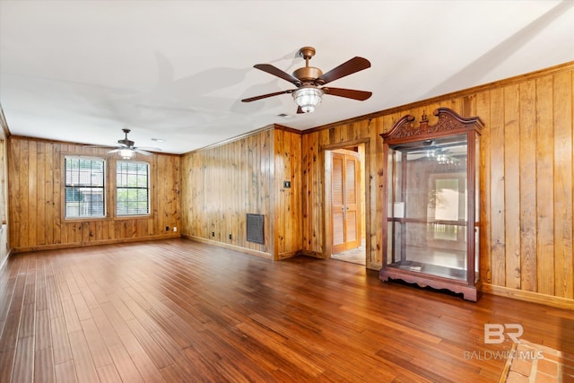 unfurnished living room featuring crown molding, wood walls, wood-type flooring, and ceiling fan