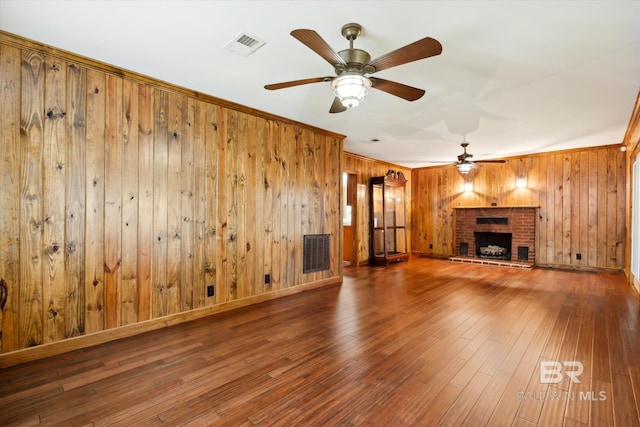 unfurnished living room with wood-type flooring, ornamental molding, a brick fireplace, ceiling fan, and wood walls