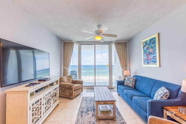 living room with ceiling fan, a water view, light tile patterned flooring, a textured ceiling, and a wall of windows