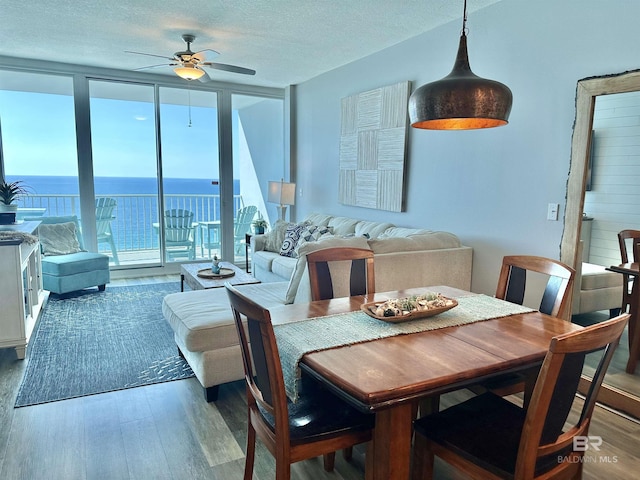 dining space with a ceiling fan, wood finished floors, a water view, a textured ceiling, and floor to ceiling windows