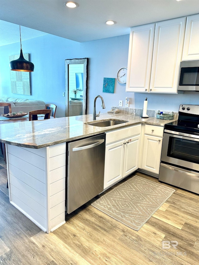 kitchen featuring light wood finished floors, white cabinets, a peninsula, stainless steel appliances, and a sink