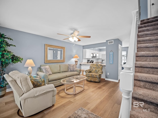 living area featuring a ceiling fan, baseboards, visible vents, stairs, and light wood-type flooring