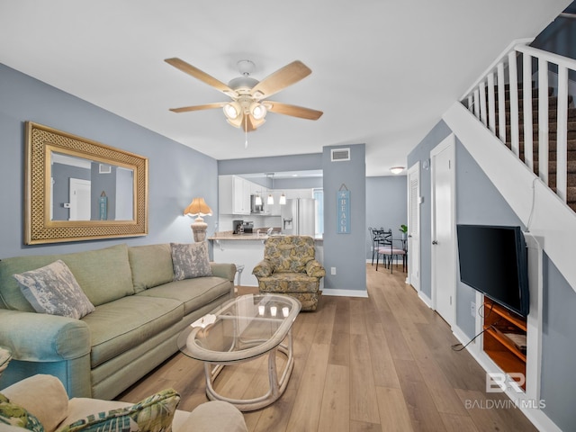 living area featuring visible vents, light wood-style flooring, baseboards, ceiling fan, and stairs