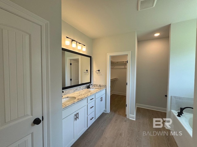 bathroom featuring a garden tub, wood finished floors, a spacious closet, visible vents, and double vanity