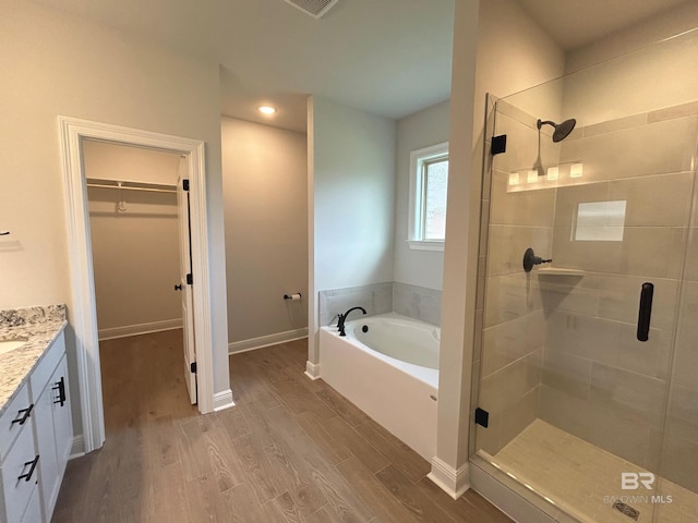 full bath with a stall shower, vanity, wood finished floors, a spacious closet, and a bath