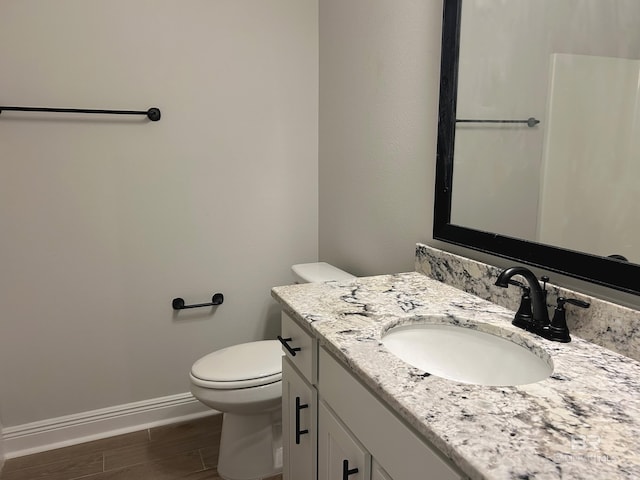 bathroom featuring baseboards, wood finished floors, toilet, and vanity