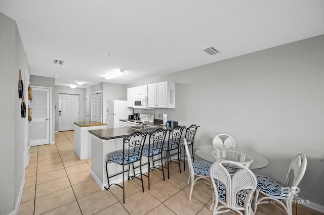 kitchen with a breakfast bar area, white appliances, light tile patterned floors, kitchen peninsula, and white cabinets